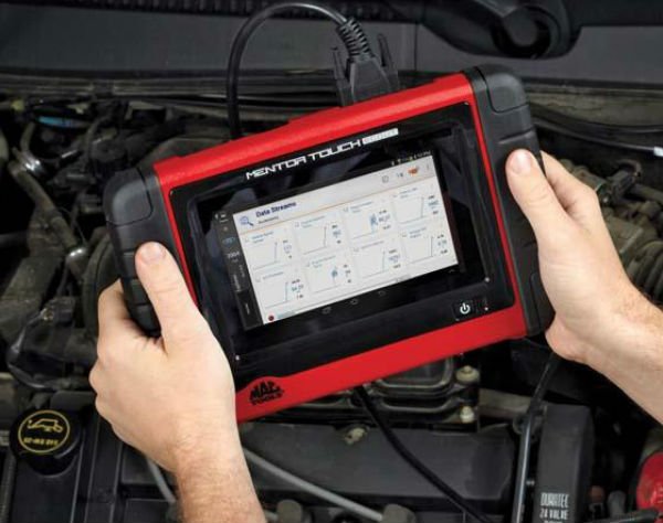 Auto mechanic using handheld automotive diagnostic tablet to troubleshoot mechanical problem.